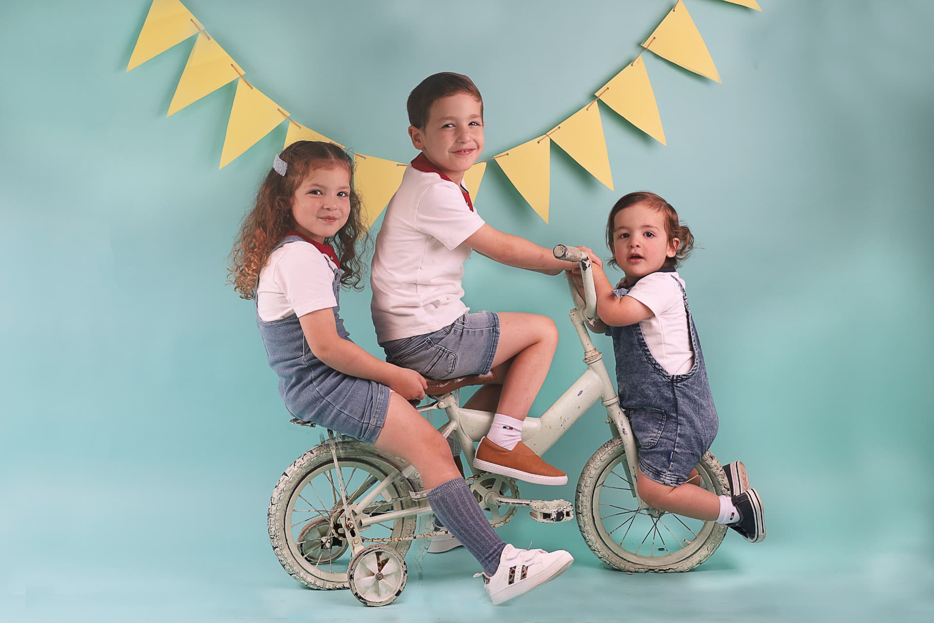 שלושה אחים רוכבים יחד על אופני וינטג' על רקע טורקיז