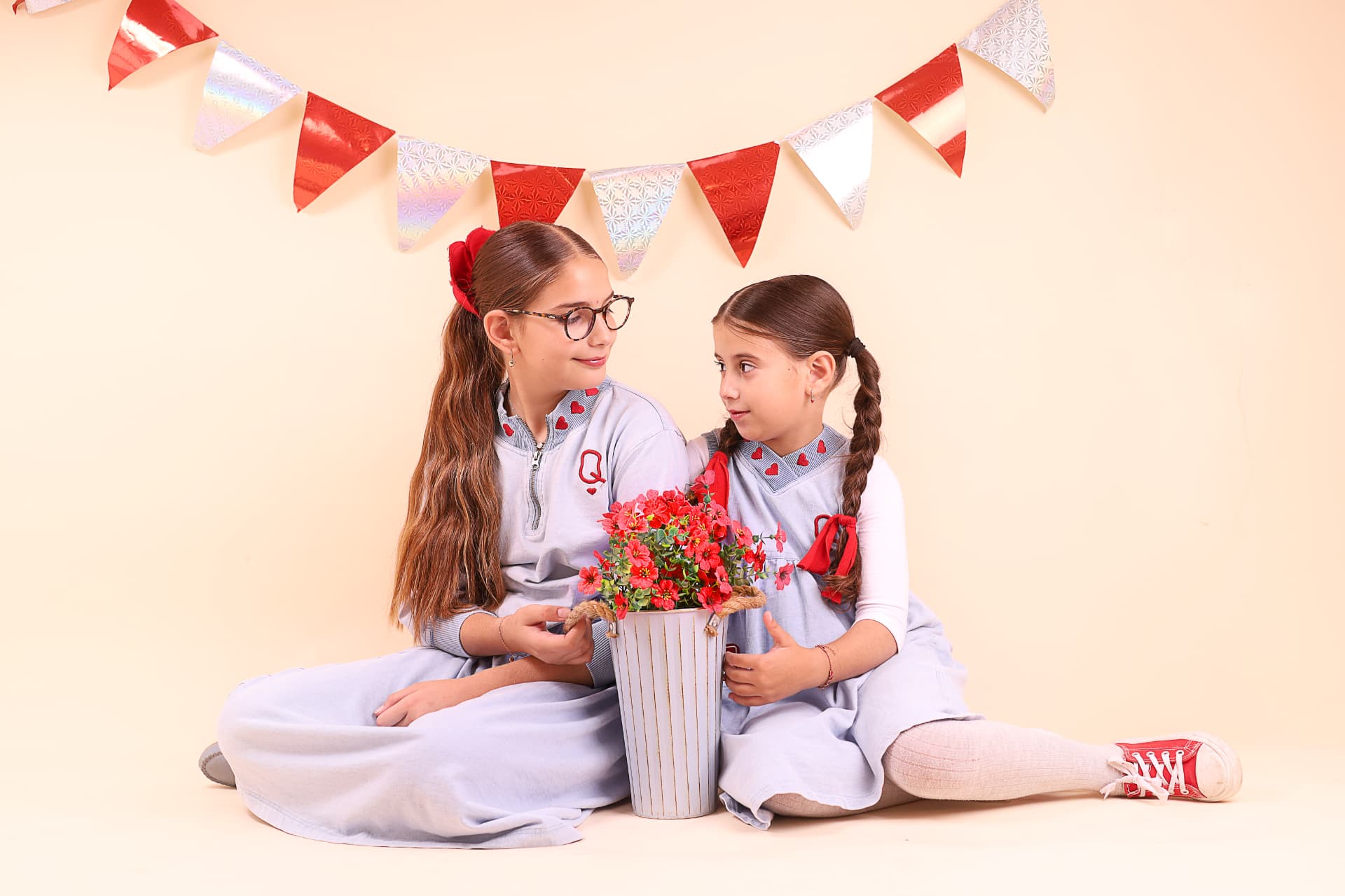 שתי אחיות יושבות על הרצפה ומחייכות זו אל מול זו ליד עציץ פרחים